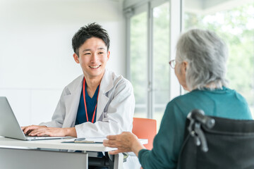 病院・介護施設で高齢者女性を笑顔で診察・問診する若いアジア人男性医師（かかりつけ医）
