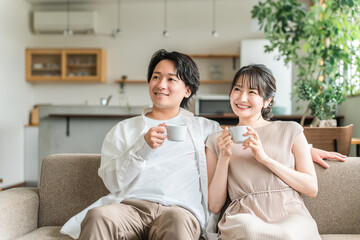 家のリビング・ソファでくつろぐ仲良しの若い日本人夫婦
