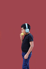 Obraz premium 9-year-old dark-skinned Latino boy with headphones eats an apple as a sign of healthy eating while listening to music