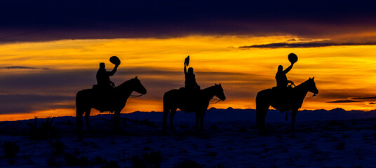 USA, Wyoming. Cowboys in silhouette against the sunset, raising their hats in greeting.