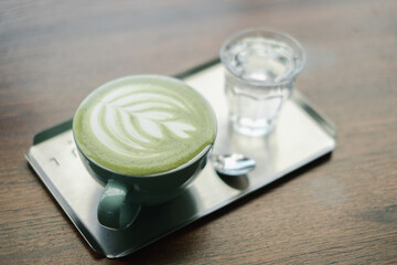 A beautifully crafted green matcha latte with intricate latte art served alongside a glass of water on a wooden table.