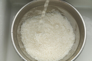 Pouring water into bowl with rice in sink, top view