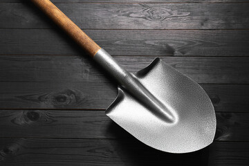 Metal shovel on black wooden table, top view