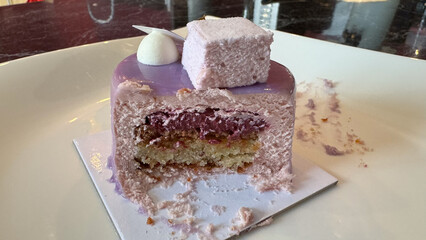 Close-up of a half-eaten purple mousse cake topped with a marshmallow, showcasing the layered interior on a white plate