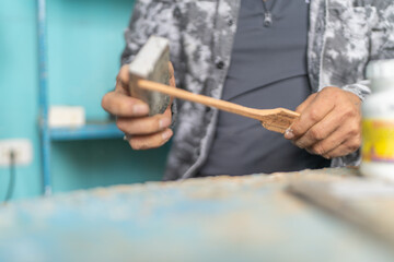 Woodcarver sanding wood piece with sandpaper in workshop