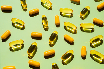 Capsules and gel pills on green background with hard shadows.