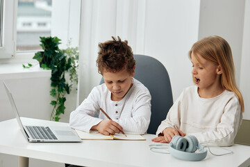 Fototapeta premium Happy children studying online at home using a laptop and tablet The boy and girl, sitting at a table in the living room, are focused and concentrated as they type and play educational games With