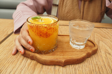 A Refreshing Orange Cocktail served beautifully alongside Water on an Elegant Wooden Platter