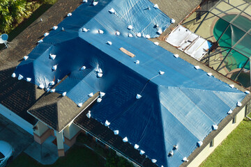 Hurricane Ian damaged house rooftop covered with protective plastic tarp against rain water leaking...