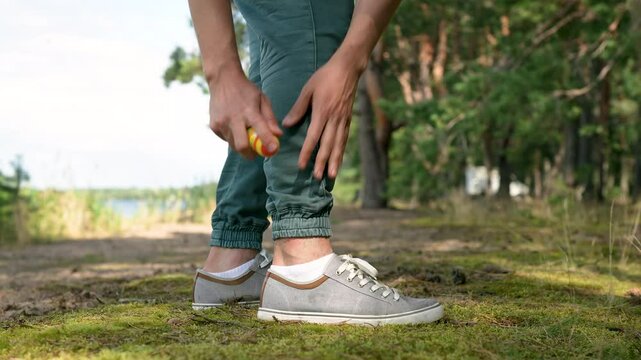 Unrecognizable man hands spray insect repellent on ankles outdoors during hike, mosquitoes, midges, horseflies bite skin. Biting insects leave marks on legs, itching, swelling, allergic reactions