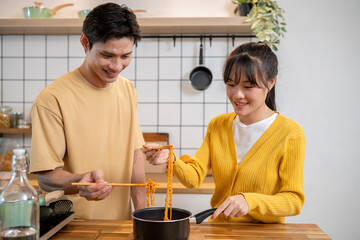 A lovely young Asian couple is eating instant noodles together at the kitchen table.