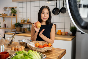 An attractive Asian female food blogger is cooking in front of the camera, recording in her kitchen.