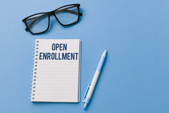 Open enrollment concept with pen, glasses, and notebook on blue background.