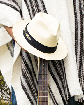 Back view of faceless man with long wavy hair wearing white wool poncho with black stripes and traditional straw hat in Cuenca, Ecuador. Cultural fashion and identity concept.