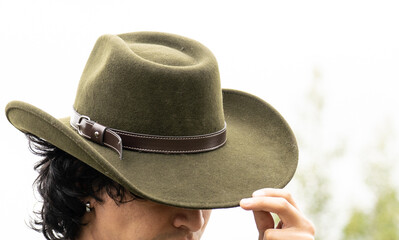 Mestizo male model with curly hair wearing blue shirt and wool cowboy hat with leather decoration. Portrait with blurred natural background and contemporary Andean cultural style.