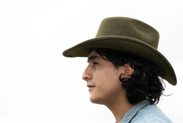 Mestizo male model with curly hair wearing blue shirt and wool cowboy hat with leather decoration. Portrait with blurred natural background and contemporary Andean cultural style.