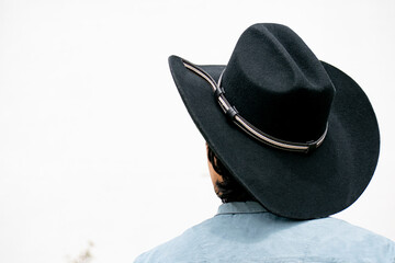 Mestizo male model with curly hair wearing blue shirt and wool cowboy hat with leather decoration. Portrait with blurred natural background and contemporary Andean cultural style.
