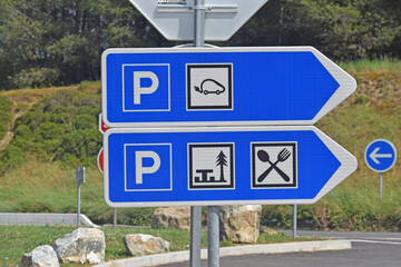 Panneaux de signalisation routière : flèches vers parkings, bornes de recharges électriques, aire de pique-nique, restaurants.