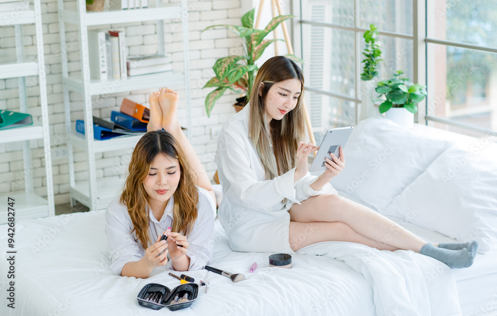 Poster Two happy beautiful Asian female girlfriends cosmetics make face take care of skin beauty products, Pretty woman watching tablet relaxed on a white bed, Concept teenage or friends lifestyle at home.