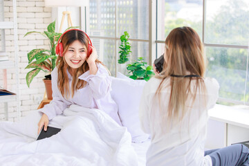 Two funny happy friends, Asian young woman pretty female smiling enjoying holding a vintage camera and taking photo of friend while sitting in bed. Concept teenage lifestyle hobby and art photography