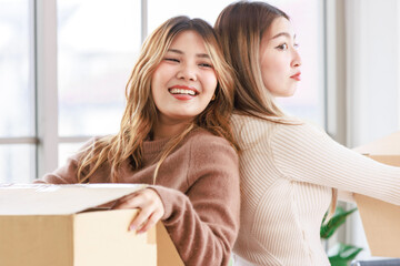 Portrait two roommates happy young Asian female moving packing things in box into new apartment,...