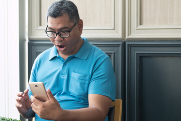 Excited happy smiling old asian senior man using smartphone with joy