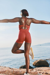 Woman exercising by the sea in a vibrant orange outfit, enjoying a peaceful moment with arms outstretched