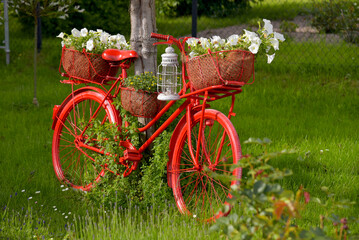 Fototapeta premium rotes Fahrrad mit Blumenbepflanzung als Dekoration im Garten