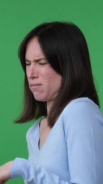 Displeased and annoyed Caucasian middle aged woman smelling disgust, nasty or unpleasant odor, standing on green background. Vertical video.