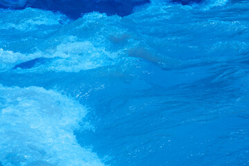 Blue water with ripples on the surface. Defocus blurred transparent blue colored clear calm water surface texture with splashes and bubbles. Water waves with shining pattern texture background.