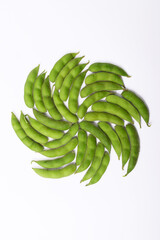 Fresh edamame pods are arranged in a swirling spiral pattern against a white background