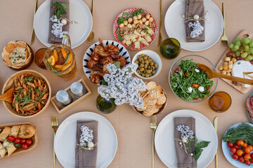 Overhead view of a beautifully arranged Mediterranean feast including assorted vegetables, olives, bread, and chicken. Table set with plates, napkins, and utensils