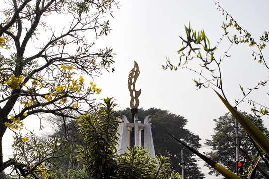 The Kujang Monument in Cianjur, West Java, Indonesia, is surrounded by lush green trees and yellow flowers. The kujang is a bladed weapon native to the Sundanese people of Indonesia.