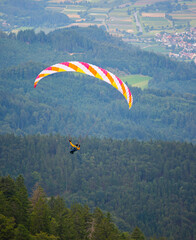 an unrecognizable person is flying on a paraglider in the mountains between hills, the city in the...