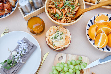 Delicious Mediterranean-inspired brunch spread featuring fresh fruit, pasta salad with vegetables, and artisanal bread arranged on wooden table without natural light