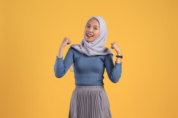 happy asian indonesian muslim woman cheerful expression with clenched fist on isolated yellow background