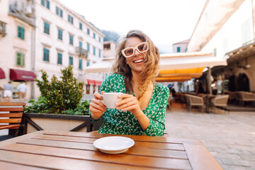 Young woman enjoying coffee at a cozy outdoor café in Kotor, Montenegro during a sunny afternoon surrounded by historical architecture. Food and drink.