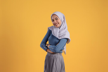 portrait of happy asian indonesian muslim woman with arm crossed on isolated yellow background