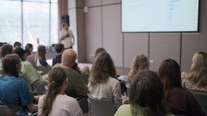 Speaker presents data to a diverse group of professionals in a business seminar setting. The audience attentively focuses on the presentation, engaging in a collaborative environment.
