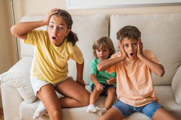 Three Children Watch TV At Home,  With Excitement. Their Positive Emotions And Lively Energy Capture A Happy And Fun Childhood Moment.