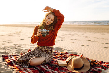 A young woman enjoying a sunny day at the beach while taking photos with her camera, captured in the warm light of the late afternoonю . Travel, blogging, technology concept.