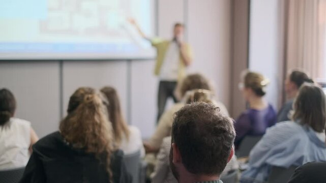 Group of people engaged in a presentation, focusing on the speaker delivering information in a conference setting.