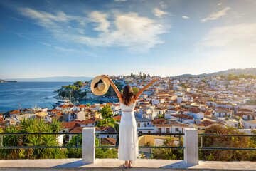 A happy tourist woman enjoys the beautiful summer sunset view of the town of Skiathos island, Sporades, Greece