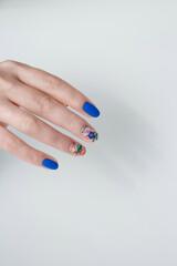 Nail art with blue gel varnish and floral design on woman's hand. Manicure salon service. White background, copy space. Vertical shot