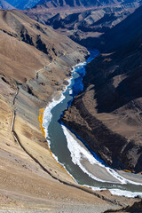 Indus river half frozen with clear water and mountain ranges on both sides.