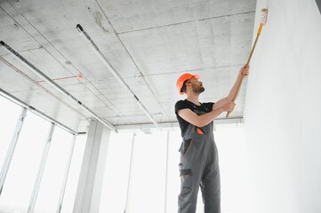 Building contractor painting grey wall with roller brush
