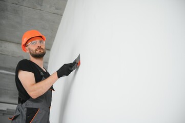 Tradesman on stilts plastering drywall in home