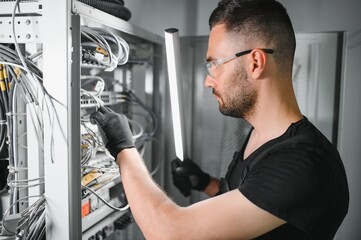 A technician works with server equipment in a data center. A man commutes wires in a server room