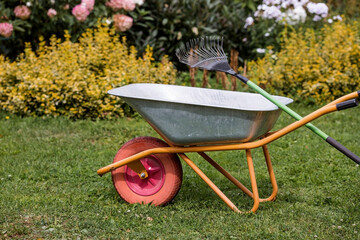 A garden wheelbarrow and a rake in the backyard of the house. The concept of housework, gardening...