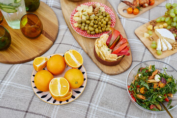 Fresh fruits, cheese, olives, and a vibrant salad arranged on a picnic blanket with wooden serving boards and glassware, creating an inviting outdoor setup for a relaxing meal